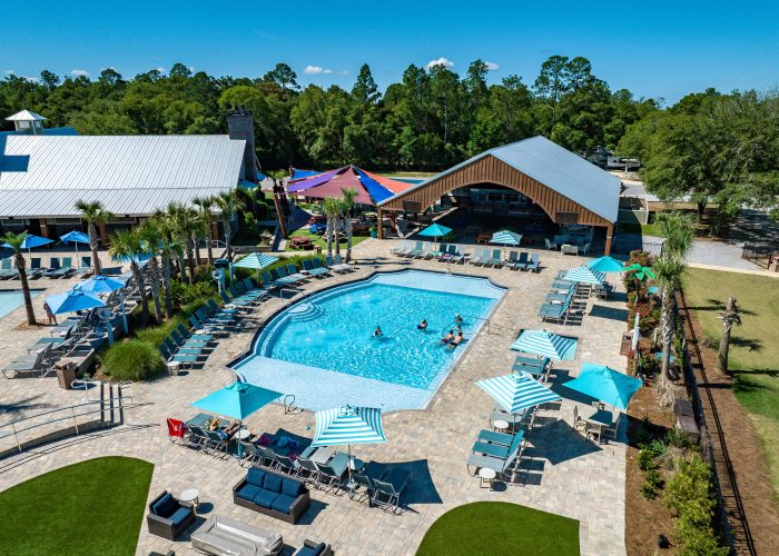 Aerial view of resort-style pool with turquoise water, lounge chairs under teal umbrellas, wood-beamed pavilion and shade sails at Splash RV Resort in Milton, Florida.