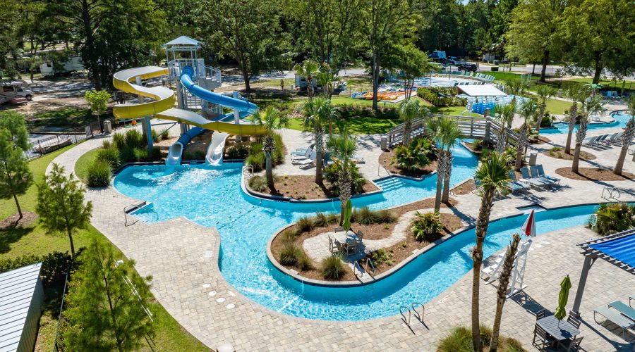 Aerial view of vibrant water park with twisting yellow and blue slides, lazy river, and pool area at Splash RV Resort in Milton, Florida.