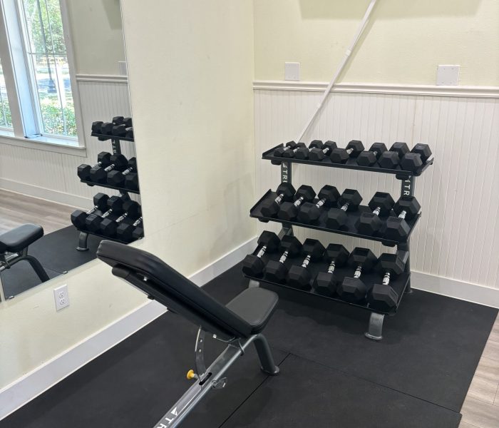 Black and gray True adjustable weight bench on rubber mat with hexagonal dumbbell rack and wall-mounted TV at a gym with pale yellow walls and white wainscoting at Splash RV Resort in Milton, Florida.