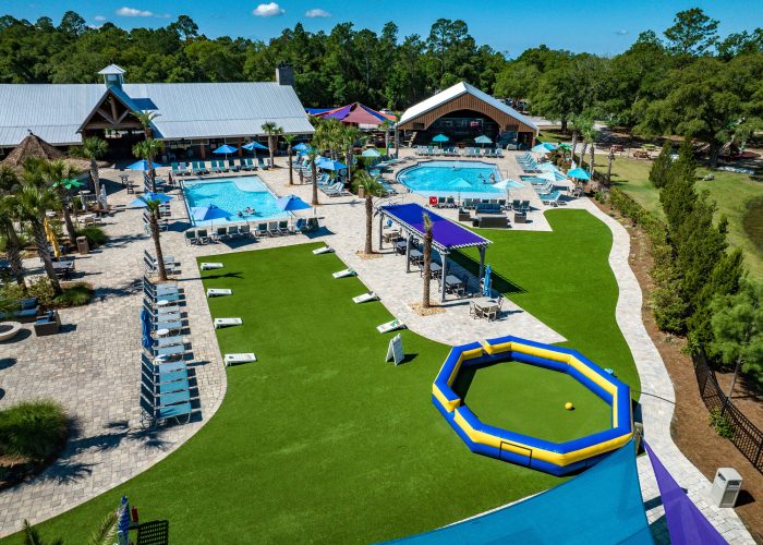 Aerial view of Splash RV Resort swimming pools surrounded by lounge chairs and umbrellas with cornhole games and gaga ball pit