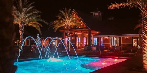 Splash RV Resort nighttime pool with vibrant turquoise and pink LED lit fountain jets and illuminated clubhouse